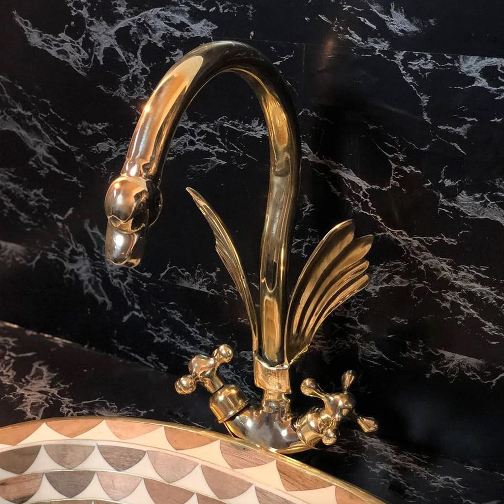 Polished brass swan-shaped bathroom faucet with intricate detailing, set against a black marble wall and paired with a decorative basin