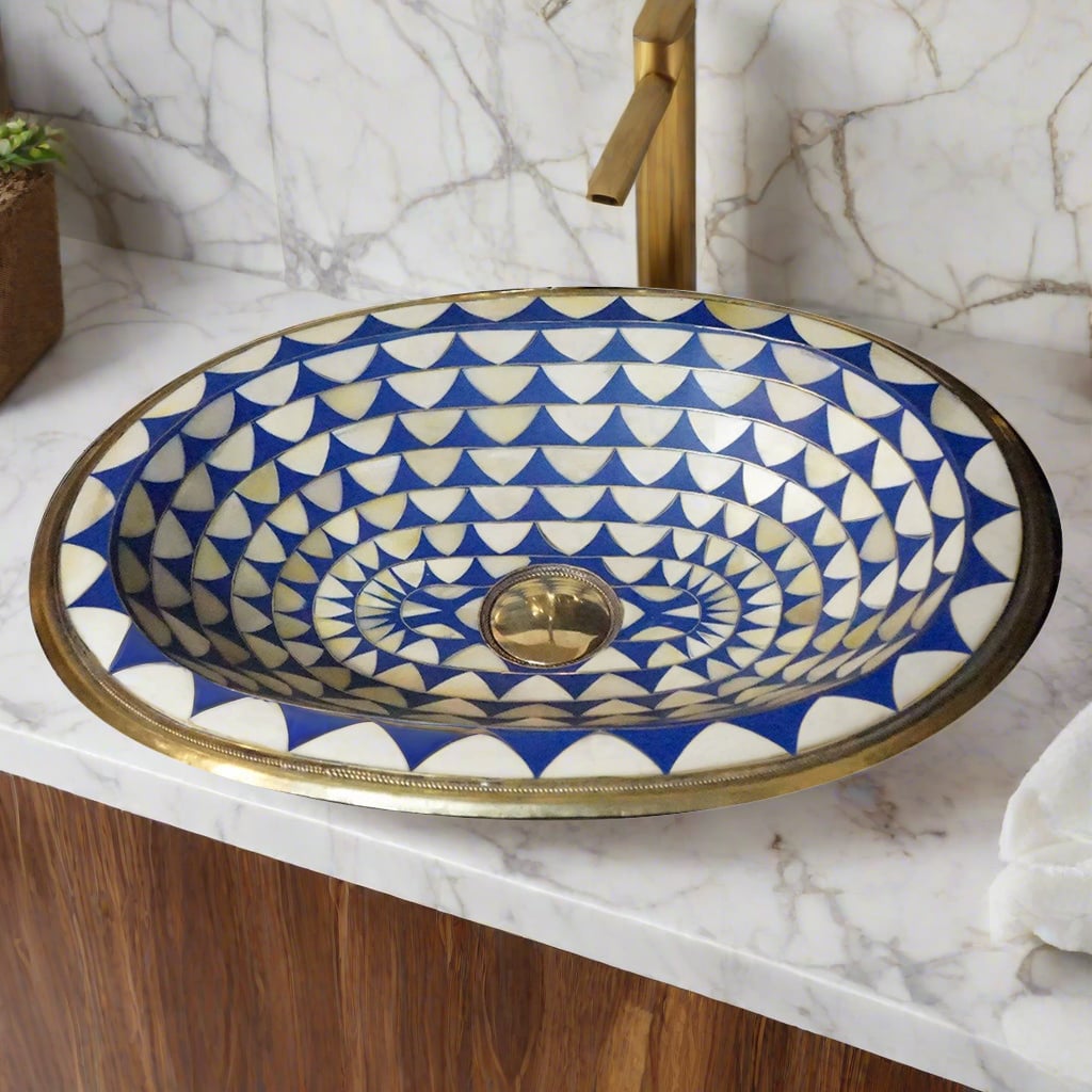 Top view of a handcrafted Moroccan brass bathroom sink with a blue and white geometric pattern, installed on a marble countertop
