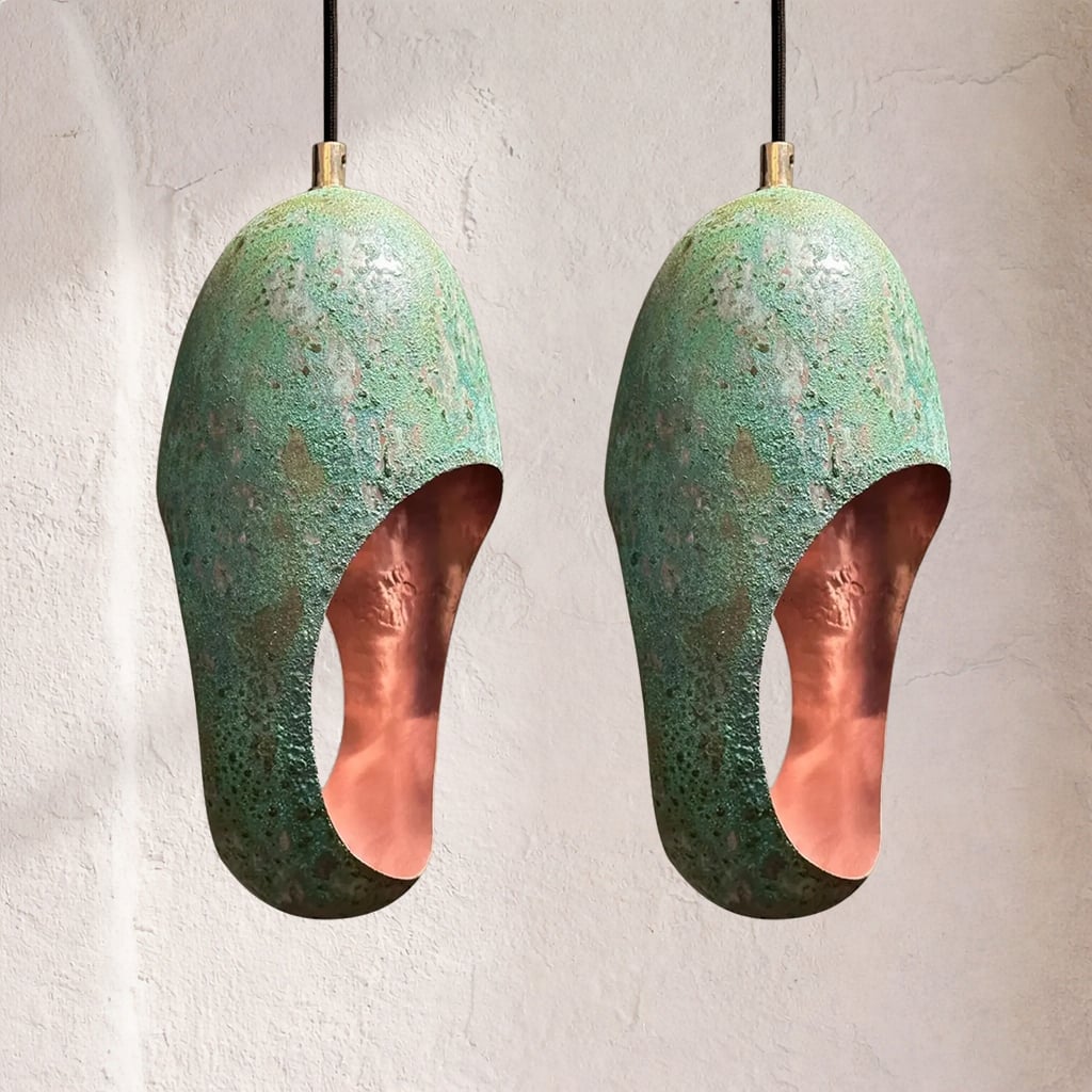 Two patinated copper pendant lamps with oxidized green surfaces and oval cutouts, mottled corrosion texture, suspended side by side