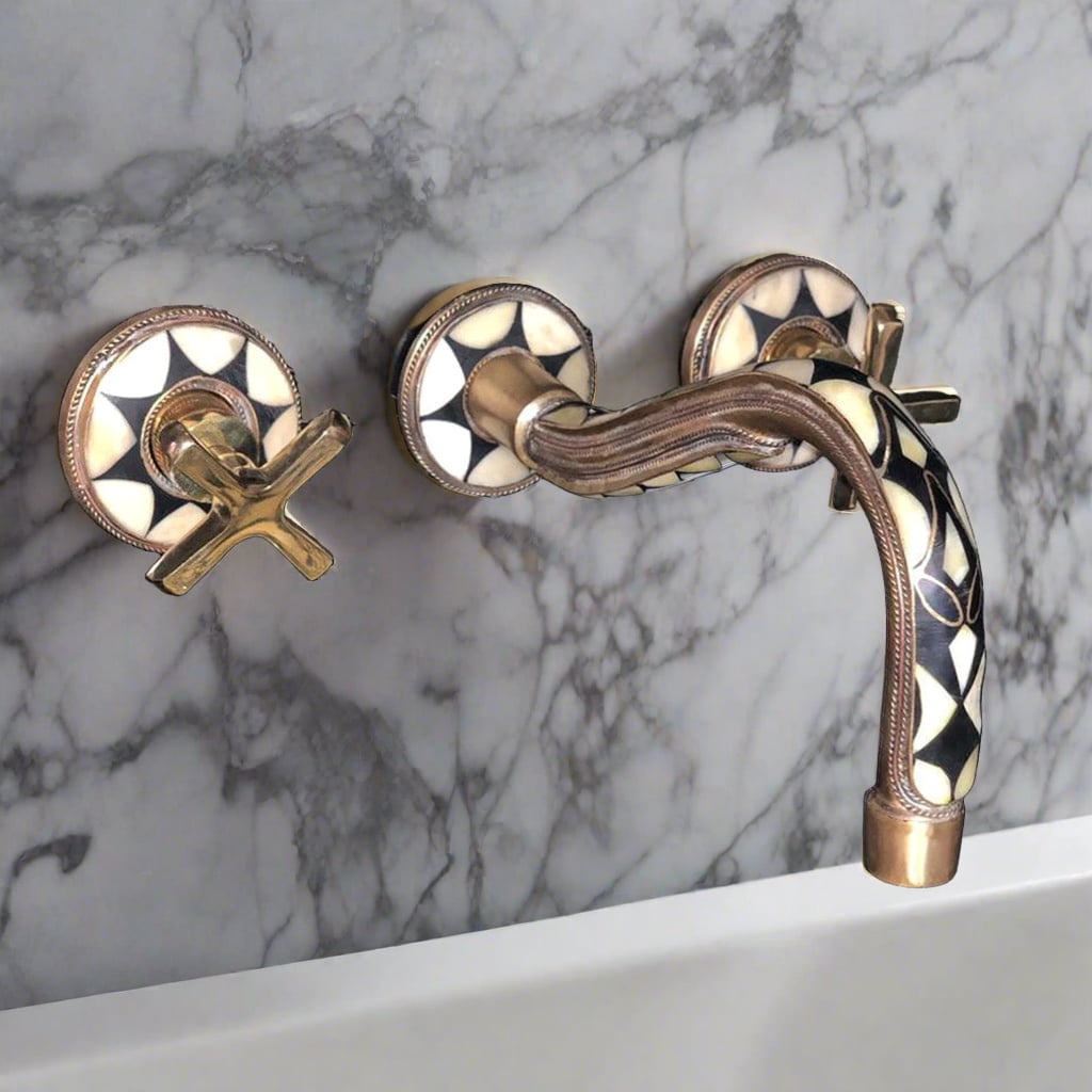 Close-up of a mounted gold bathroom faucet with decorative elements and cross handles against a marble wall