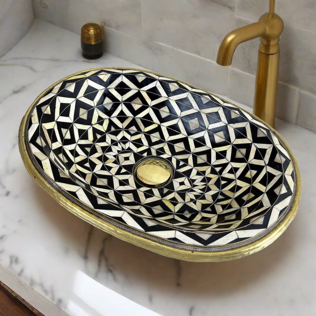 Top view of a handcrafted Moroccan bathroom basin featuring intricate black, white, and gold geometric patterns with brass inlay, set on a marble countertop