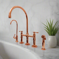 Copper kitchen bridge faucet set with a tall gooseneck spout, side sprayer, and filtered water tap on a marble countertop