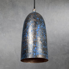 Hammered copper cylindrical pendant lamp with blue patina finish and mottled texture, suspended from black cord, interior unlit