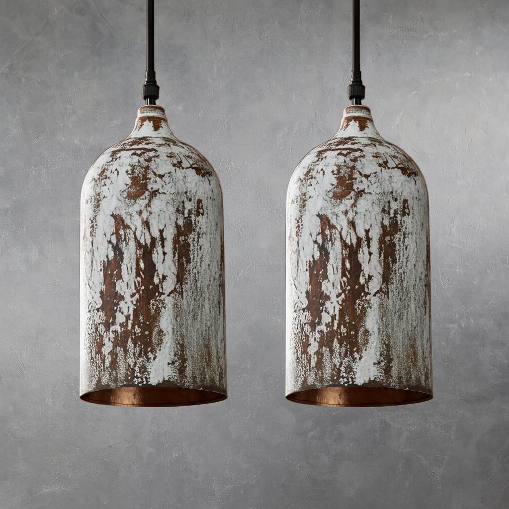 Two cylindrical metal pendant lamps with distressed white painted finish and exposed brown areas, hanging side by side from black cords