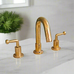 Three-hole widespread bathroom faucet with aged brass finish and modern lever handles, installed on a white marble countertop