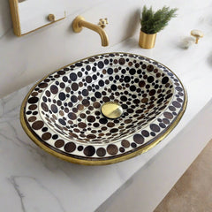 Top view of a handcrafted brass drop-in sink with a black and white mosaic design, installed on a marble countertop in a modern bathroom