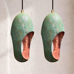 Two patinated copper pendant lamps with oxidized green surfaces and oval cutouts, mottled corrosion texture, suspended side by side