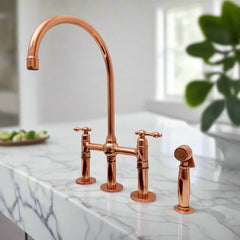 Polished copper bridge kitchen faucet with side sprayer installed on white marble countertop in a bright modern kitchen