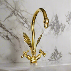 Ornate brass swan-neck faucet with feather detailing and traditional knob handles on marble countertop