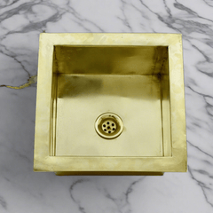 Close-up of a handcrafted brass kitchen sink, highlighting the polished brass material and square design suitable for undermount installation