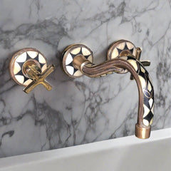 Close-up of a mounted gold bathroom faucet with decorative elements and cross handles against a marble wall